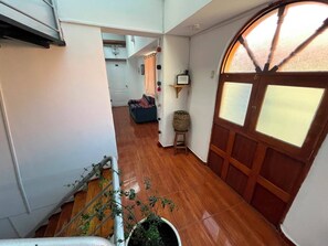 Un pasillo con piso de madera, una planta en maceta, una escalera y una puerta con ventana.