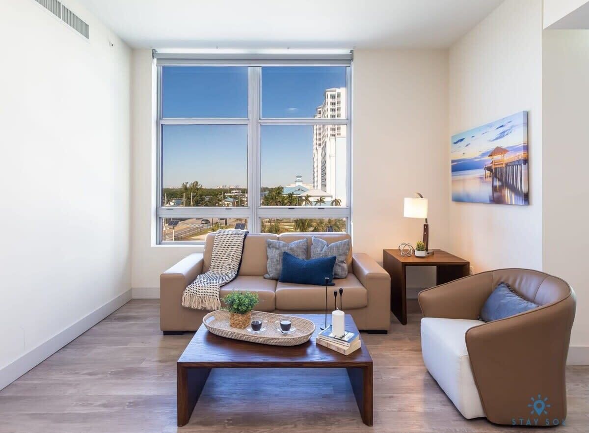 A modern living room with a large window, a sofa, a coffee table, and a painting on the wall.