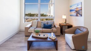 A modern living room with a large window, a sofa, a coffee table, and a painting on the wall. - Modern Condo Stay Sun Deck - Rooftop Infinity Pool (Hollywood)