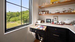 Una cocina con un amplio ventanal, estantes de madera y diversos utensilios de cocina.