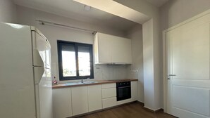 A kitchen with white cabinets, a black oven, and a window with blinds. - Cozy 1-bedroom apartment with sea view (Saranda)