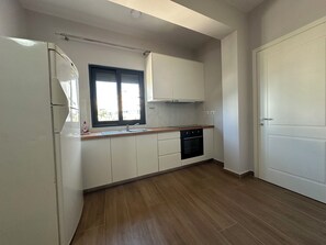 A kitchen with white cabinets, a black oven, and a window with blinds. - Cozy 1-bedroom apartment with sea view (Saranda)
