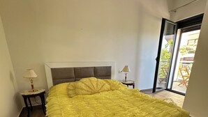 A bedroom with a large bed, two bedside tables with lamps, a sliding glass door to the outside, and a ceiling light fixture. - Cozy 1-bedroom apartment with sea view (Saranda)