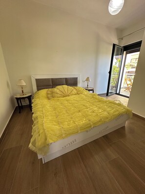 A bedroom with a large bed, two bedside tables with lamps, a sliding glass door to the outside, and a ceiling light fixture. - Cozy 1-bedroom apartment with sea view (Saranda)