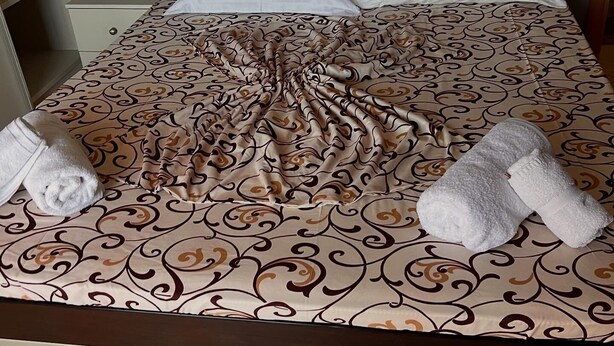 A neatly made bed with a patterned bedspread, two pillows, and two towels. - Cozy 1-bedroom apartment with sea view (Saranda)