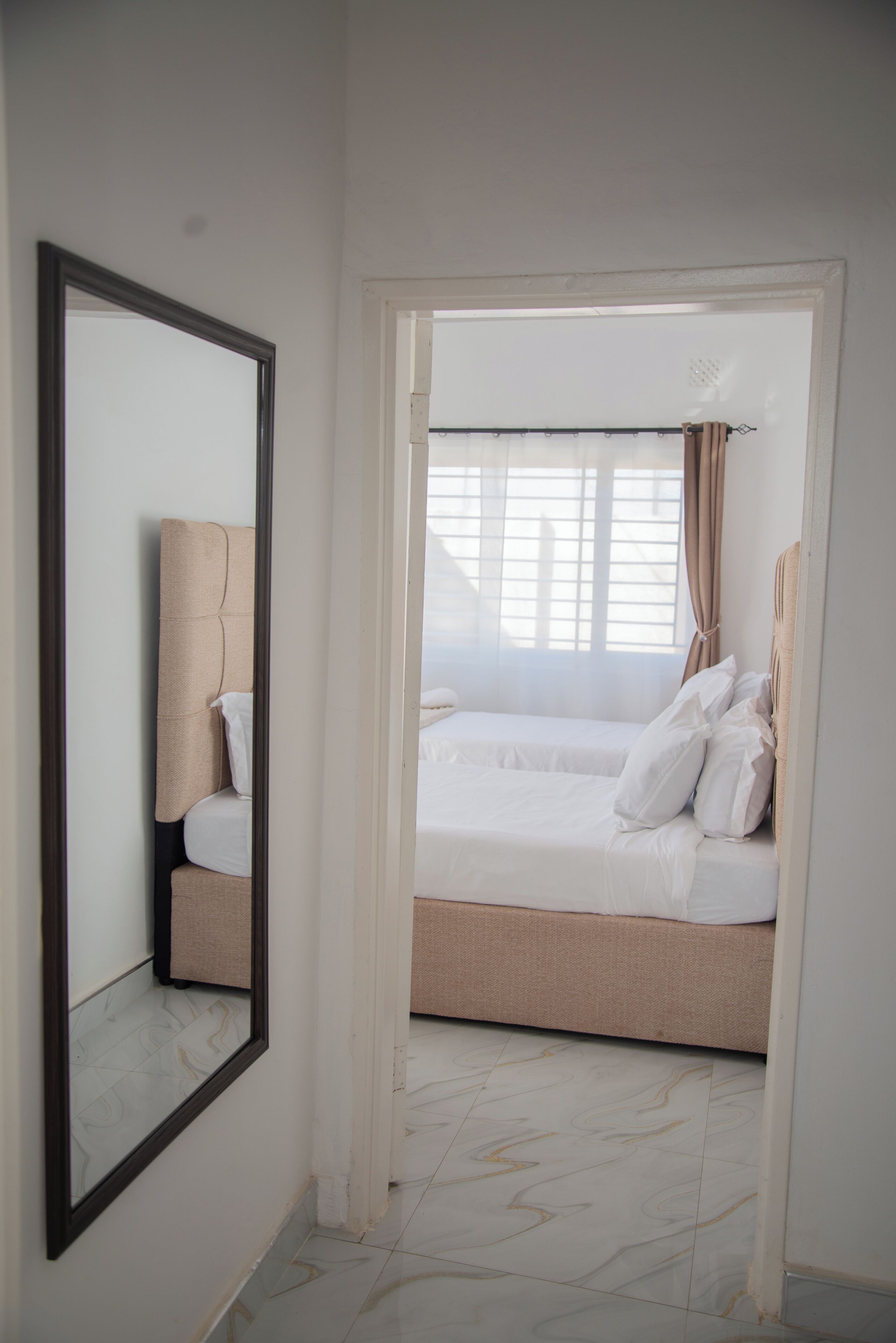 A hotel room with a large mirror, a bed with white bedding, and a view of the outside through a window with curtains.