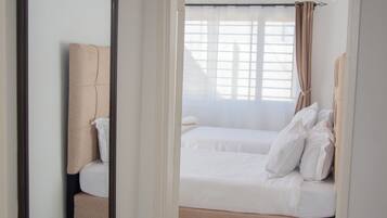 A hotel room with a large mirror, a bed with white bedding, and a view of the outside through a window with curtains.