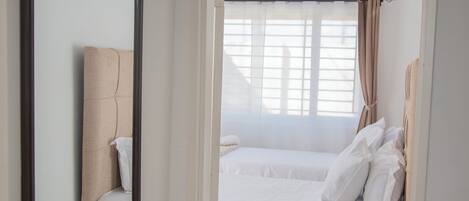 A hotel room with a large mirror, a bed with white bedding, and a view of the outside through a window with curtains.