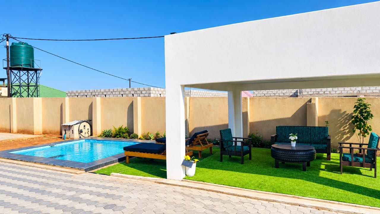 Un área de piscina moderna al aire libre con depósito de agua, césped artificial y mobiliario exterior.