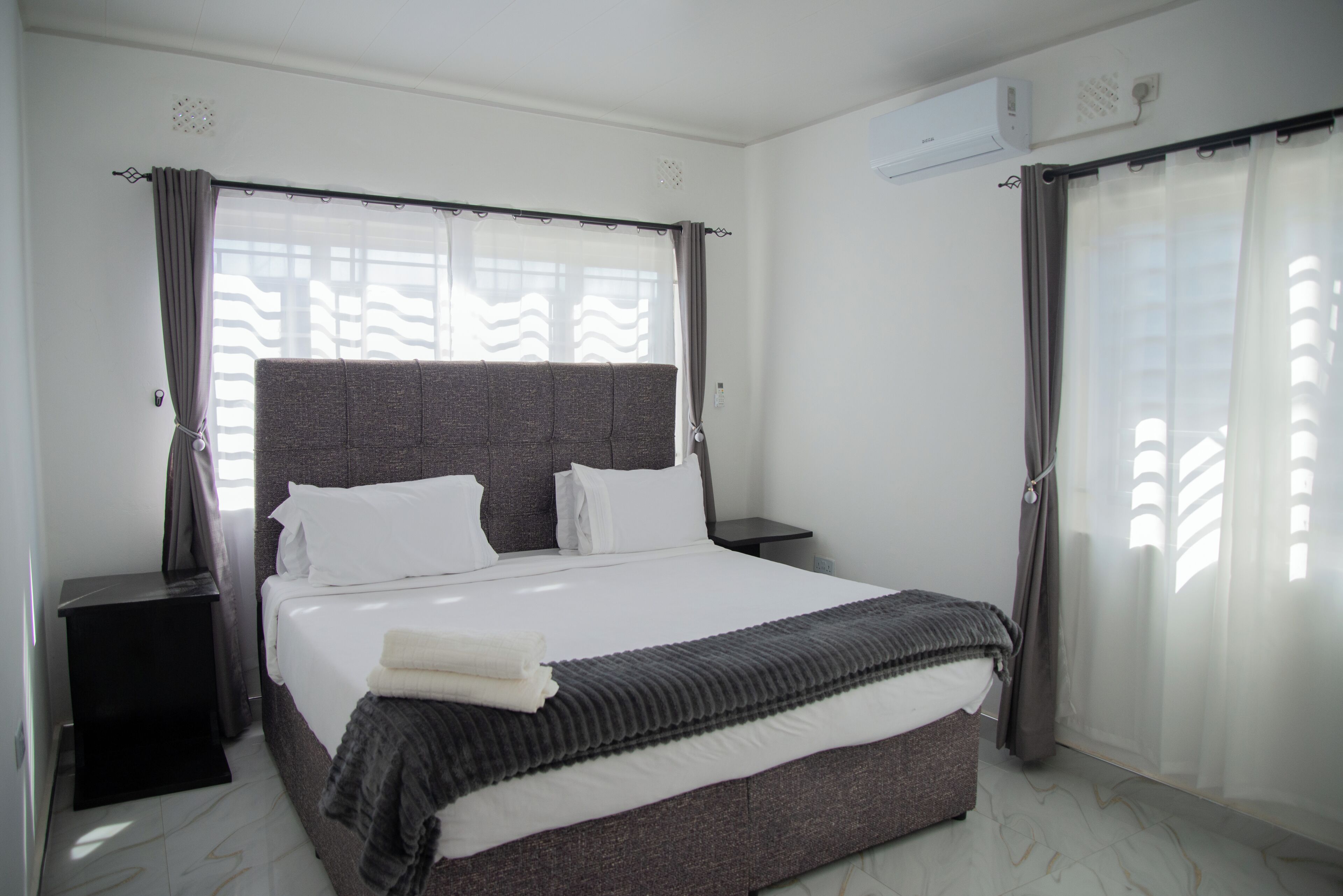 Habitación de hotel con una cama grande, una mesita de noche, un equipo de aire acondicionado y una ventana con cortinas.