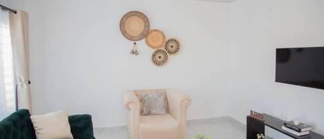 A living room with a dark green sofa, a beige armchair, a round coffee table, and a flat-screen TV mounted on the wall.