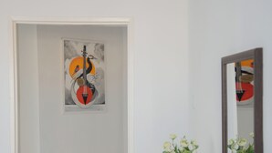 A hallway with a door leading to a room, a framed artwork on the wall, a mirror, and a vase with flowers on a table.