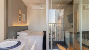 A modern hotel room with a bed, a small table with a bowl and utensils, a glass partition, and an air conditioning unit on the wall. - Studio with Pool near the Subway | Vila Mariana (São Paulo)