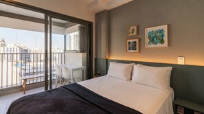 A hotel room with a large bed, a balcony with a view of the city, and two framed artworks on the wall. - Studio with Pool near the Subway | Vila Mariana (São Paulo)