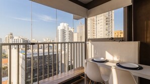 A balcony with a dining table and chairs, overlooking a cityscape with high-rise buildings. - Studio com Piscina perto do metrô Vila Mariana (São Paulo)