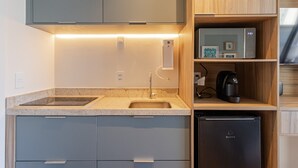 A compact kitchen with a built-in oven, a sink, and a coffee machine on a shelf. - Studio com Piscina perto do metrô Vila Mariana (São Paulo)