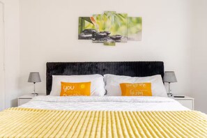A bed with two pillows, a headboard, bedside tables, and a wall-mounted artwork.