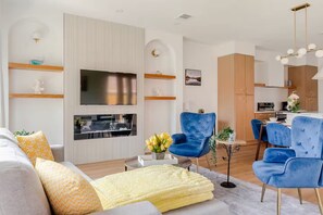 Un salon moderne doté d’un téléviseur à écran plat, de fauteuils à revêtement bleu, d’un canapé avec des coussins à motifs et d’un coin repas comprenant une table et des chaises.