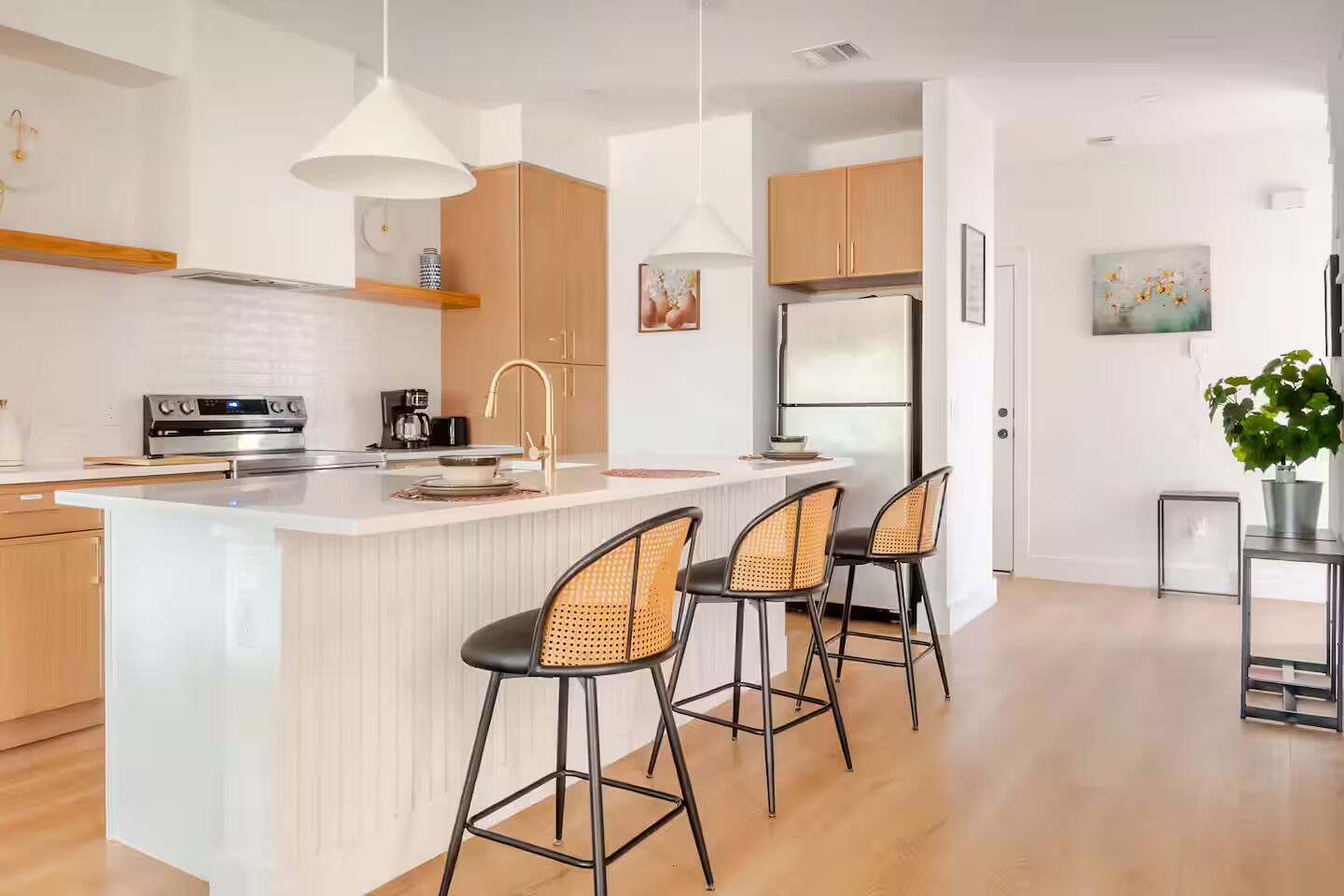Een moderne keuken met een centraal eiland, barstoelen, hanglampen en houten keukenkastjes.