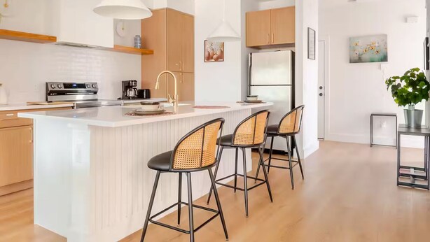 A modern kitchen with a central island, bar stools, pendant lighting, and wooden cabinetry.