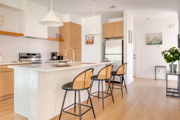 A modern kitchen with a central island, bar stools, pendant lighting, and wooden cabinetry.