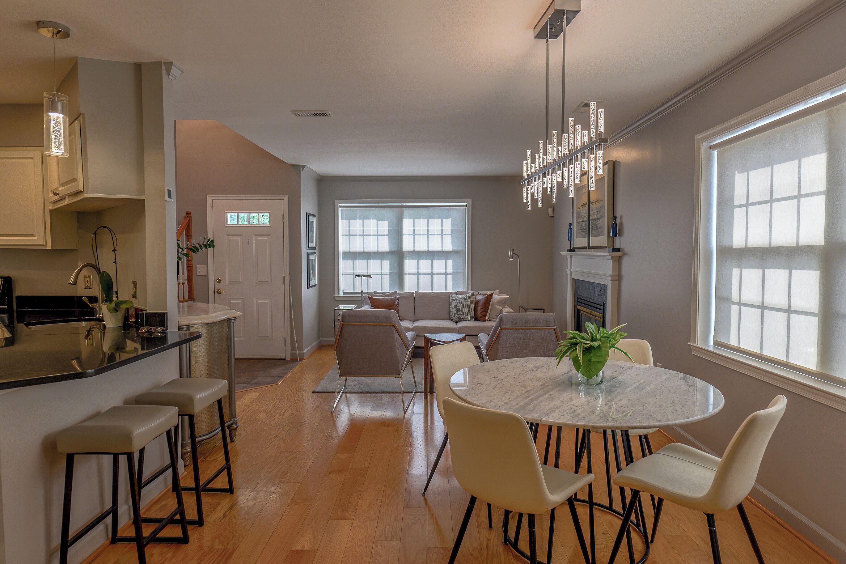 A modern kitchen with a central island, a dining area with a round table and chairs, and a living room with a sofa and a fireplace.