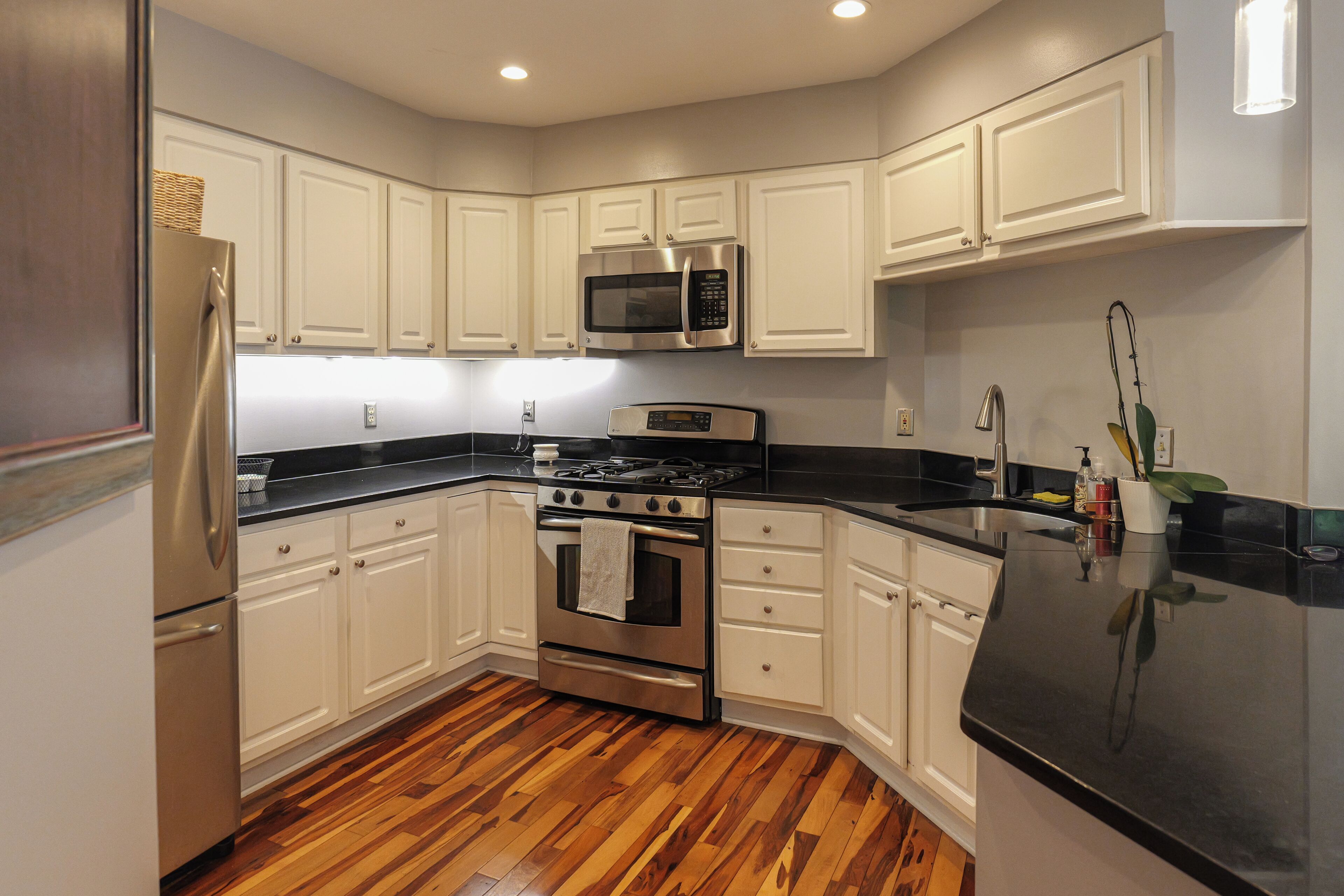 A modern kitchen with white cabinetry, stainless steel appliances, and a wooden floor.