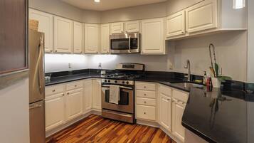 A modern kitchen with white cabinetry, stainless steel appliances, and a wooden floor.