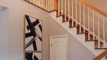 A staircase with a wooden handrail and white balusters, leading to a landing with a white door and two abstract paintings.