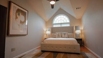 A bedroom with a large bed, a ceiling fan, a window, and a framed picture on the wall.