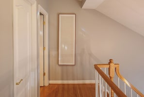 A hallway with a wooden staircase, a white door, and a framed document on the wall.