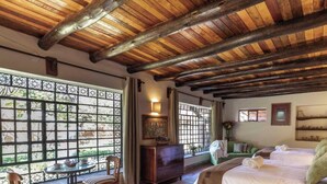 Una habitación con techo de madera, un sofá verde, una cama con ropa blanca y una ventana con celosía decorativa.