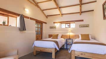 Um quarto com duas camas de madeira, uma mesinha, uma cadeira e uma janela com cortinas.