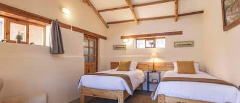 A room with two wooden beds, a small table, a chair, and a window with curtains.