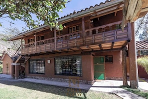 Un edificio de dos pisos con un balcón, una entrada protegida por una reja y una pequeña zona de porche.
