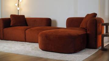 Ein Ecksofa in einem Wohnzimmer mit einem hellen Teppich und einer Stehlampe mit mehreren Lampenköpfen.