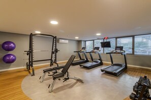 Ein Fitnessstudio mit Langhantelbank, Laufbändern, einem Squat-Stand und Kurzhanteln.