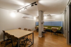 A conference room with a large table and chairs, a green sofa, and a trash bin. - Studio com Piscina Perto do Metr Vila Mariana (São Paulo)