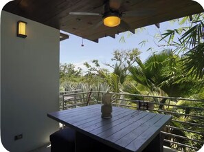 A balcony with a wooden table and a vase, overlooking a garden with various plants. - Wonderful 2-bedroom unit. Steps to West Bay Beach (Roatan)