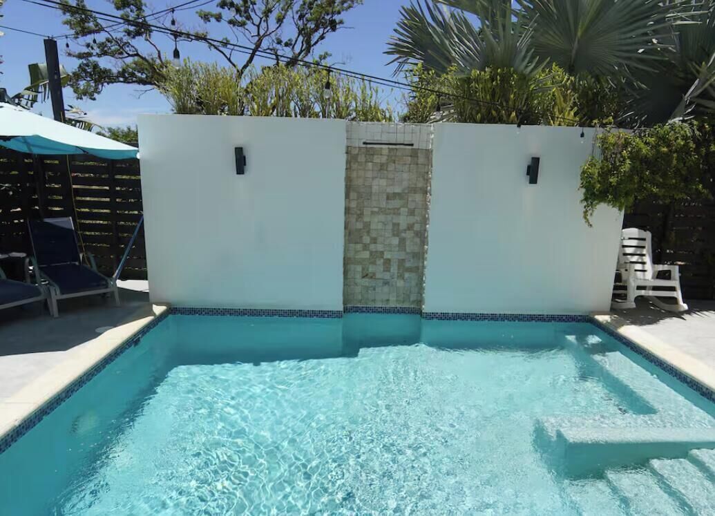Ein rechteckiger Pool mit einer Fliesenbordüre, umgeben von einer weißen Mauer mit einem kleinen, mit Fliesen versehenen Bereich.