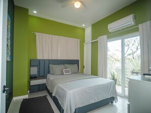Ein Schlafzimmer mit Bett, Nachttischen, Deckenventilator, Klimaanlage und Blick ins Freie.