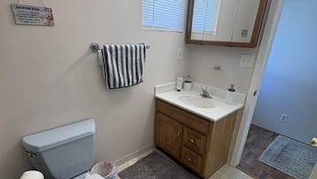A bathroom with a toilet, sink, vanity, and a mirror with lights above.