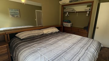 A bedroom with a bed, a ceiling fan, a mirror, and a door.