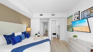 Ein modernes Schlafzimmer mit einem großen Bett, einem Nachttisch mit Lampe, einem Fernseher und Bildern an der Wand.
