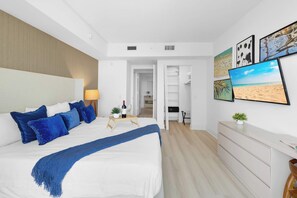 Ein modernes Schlafzimmer mit einem großen Bett, einem Nachttisch mit Lampe, einem Fernseher und Bildern an der Wand.