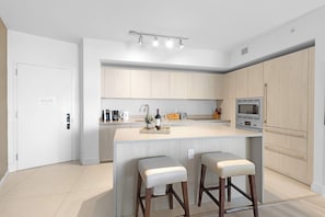 A modern kitchen with a central island, bar stools, and built-in appliances. - Modern 1BR Apartment | Pool & Ocean Views (Hollywood)