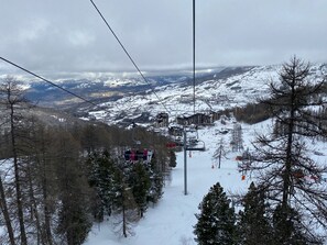 A ski lift with passengers, a snowy mountain landscape, and buildings in the background.