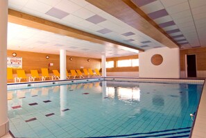 Una piscina interior con suelo y paredes de azulejos, vigas de madera y sillas amarillas a lo largo del borde.