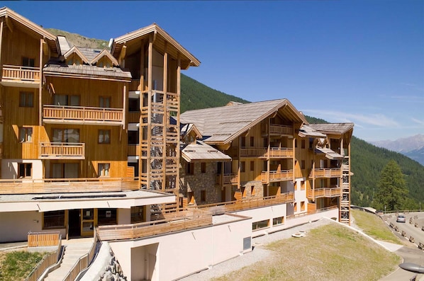 A multi-story wooden lodge with balconies, set against a mountainous backdrop.