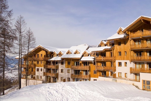 A multi-story wooden building with balconies, surrounded by snow-covered slopes and trees.